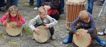 Kinder trommeln mit Begeisterung mit Issa vor dem Eingang der Odenwald-Institut-Buchhandlung auf der Tromm 